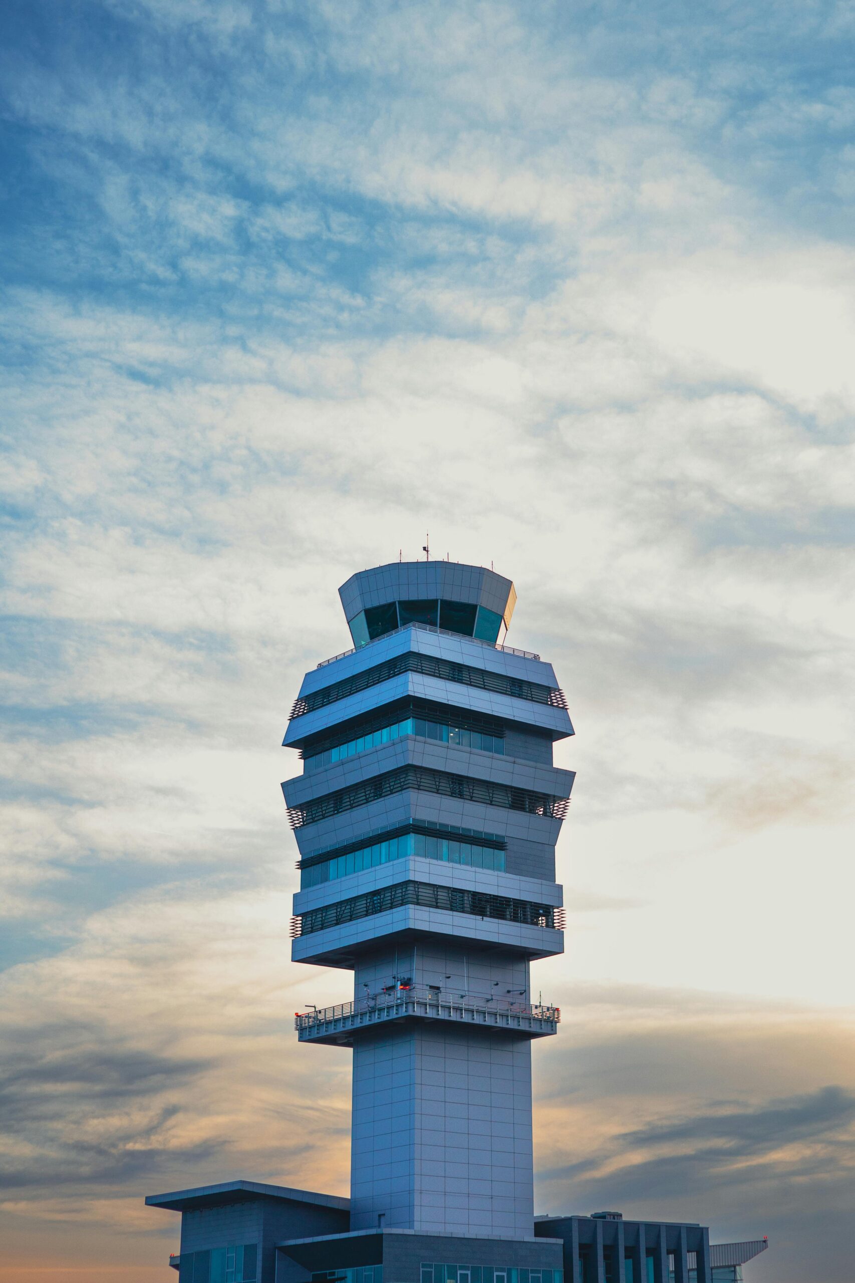 A modern airport control tower stands tall against a vibrant sky with scattered clouds, illuminated by warm light from the setting or rising sun. - TrenStar